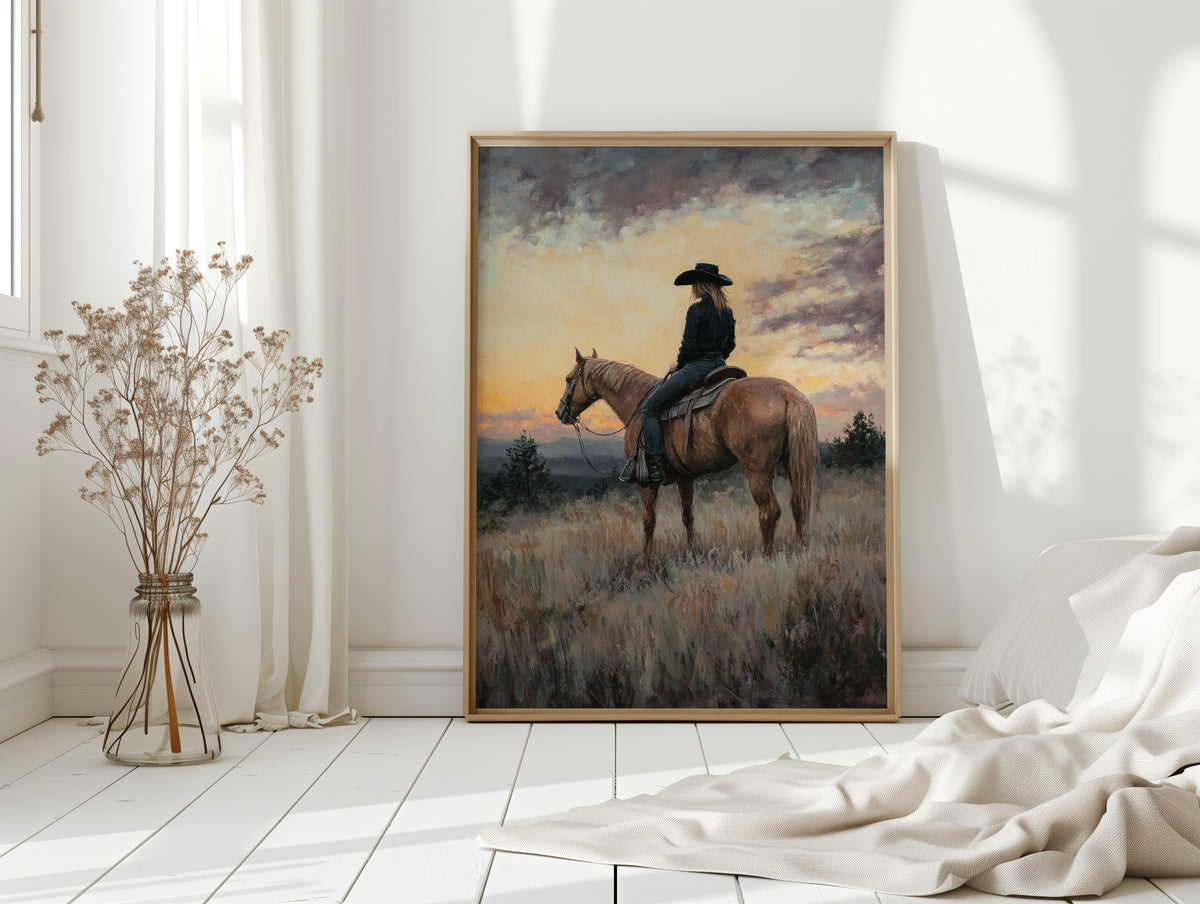 Framed painting of a person on horseback in a field with a sunset, displayed in a room with white walls and decor.