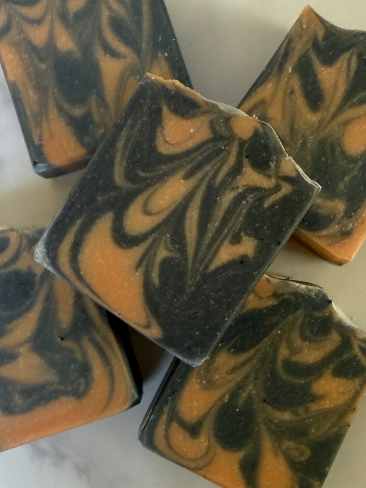 Several rectangular bars of marbled soap with a dark charcoal-black and warm orange swirl pattern, arranged on a light surface.