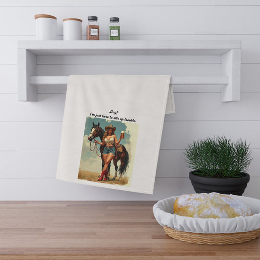 Towel with a graphic design of a woman on a horse hanging on a wall above a wooden surface with a plant and basket.