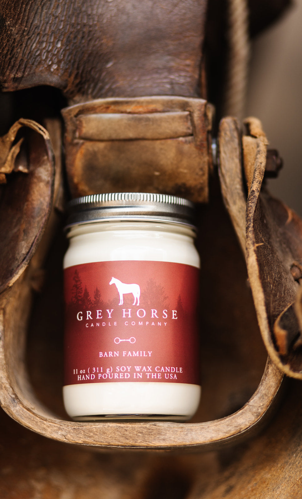 White candle jar with red label featuring 'Grey Horse Candle Company' on a rustic leather background.