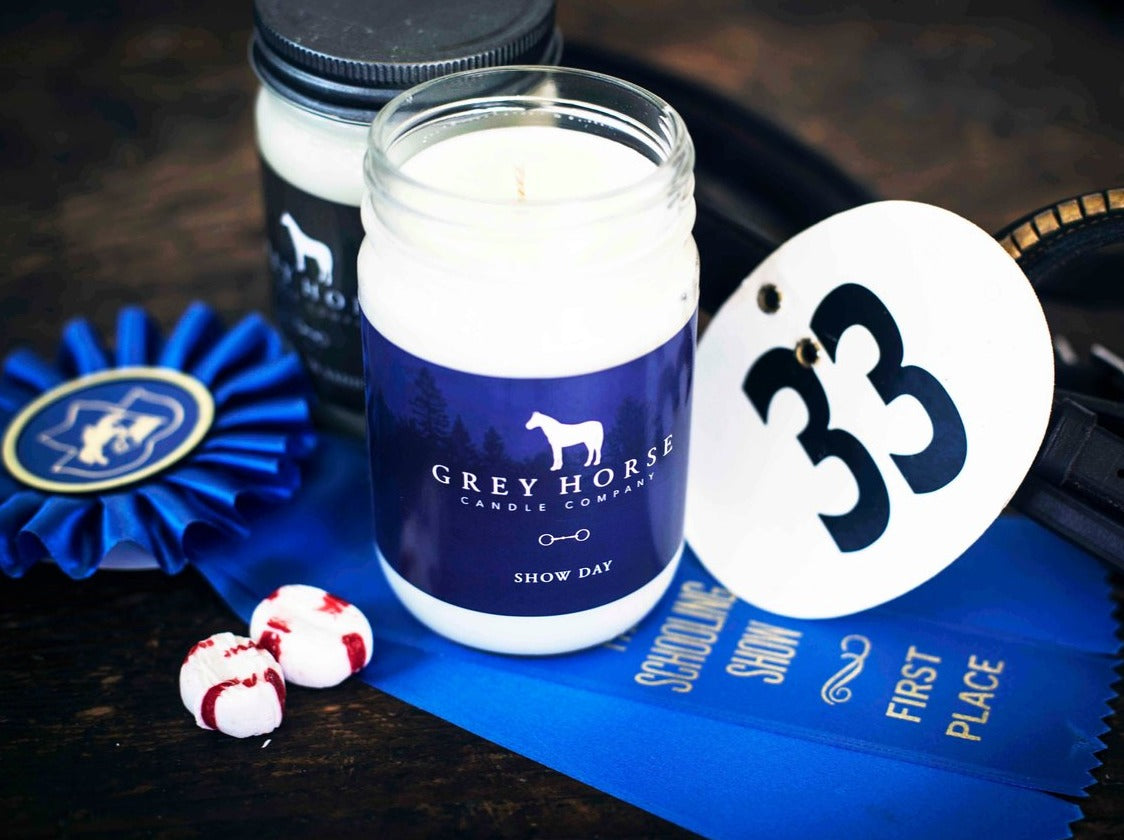 Candle with 'Grey Horse Candle Company' label on a table with ribbons and candy.
