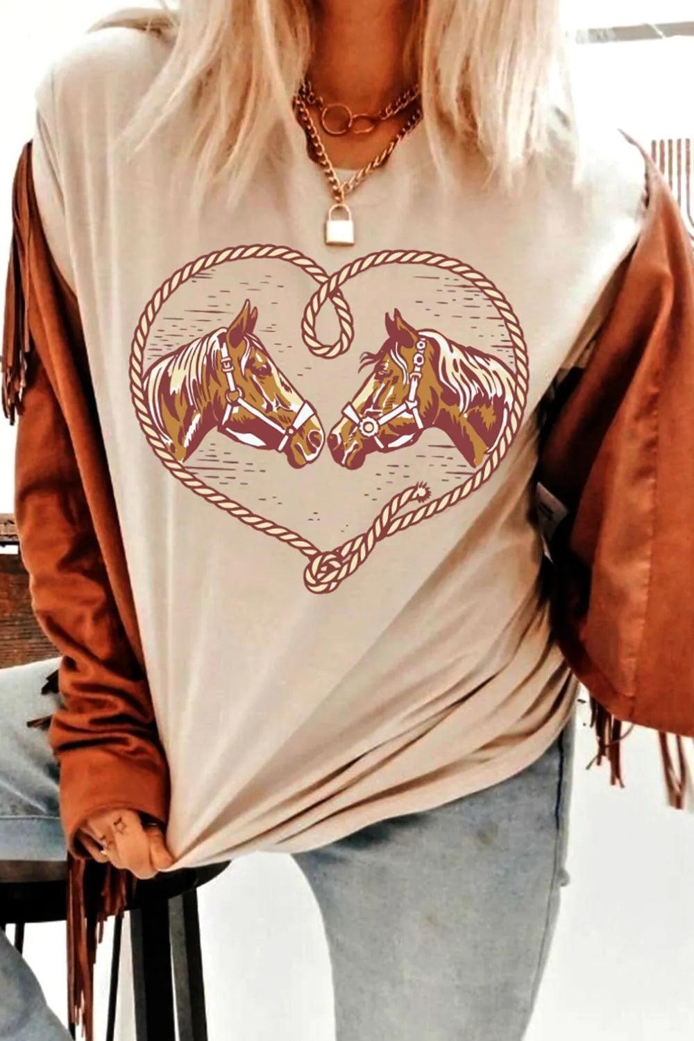 Person wearing a beige t-shirt with horse design and brown jacket indoors