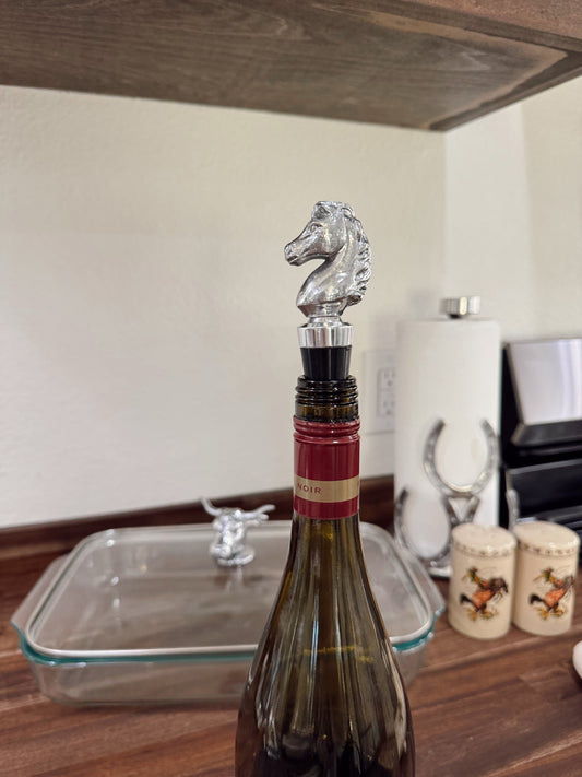 Wine bottle with a silver horse-shaped stopper on a wooden surface.