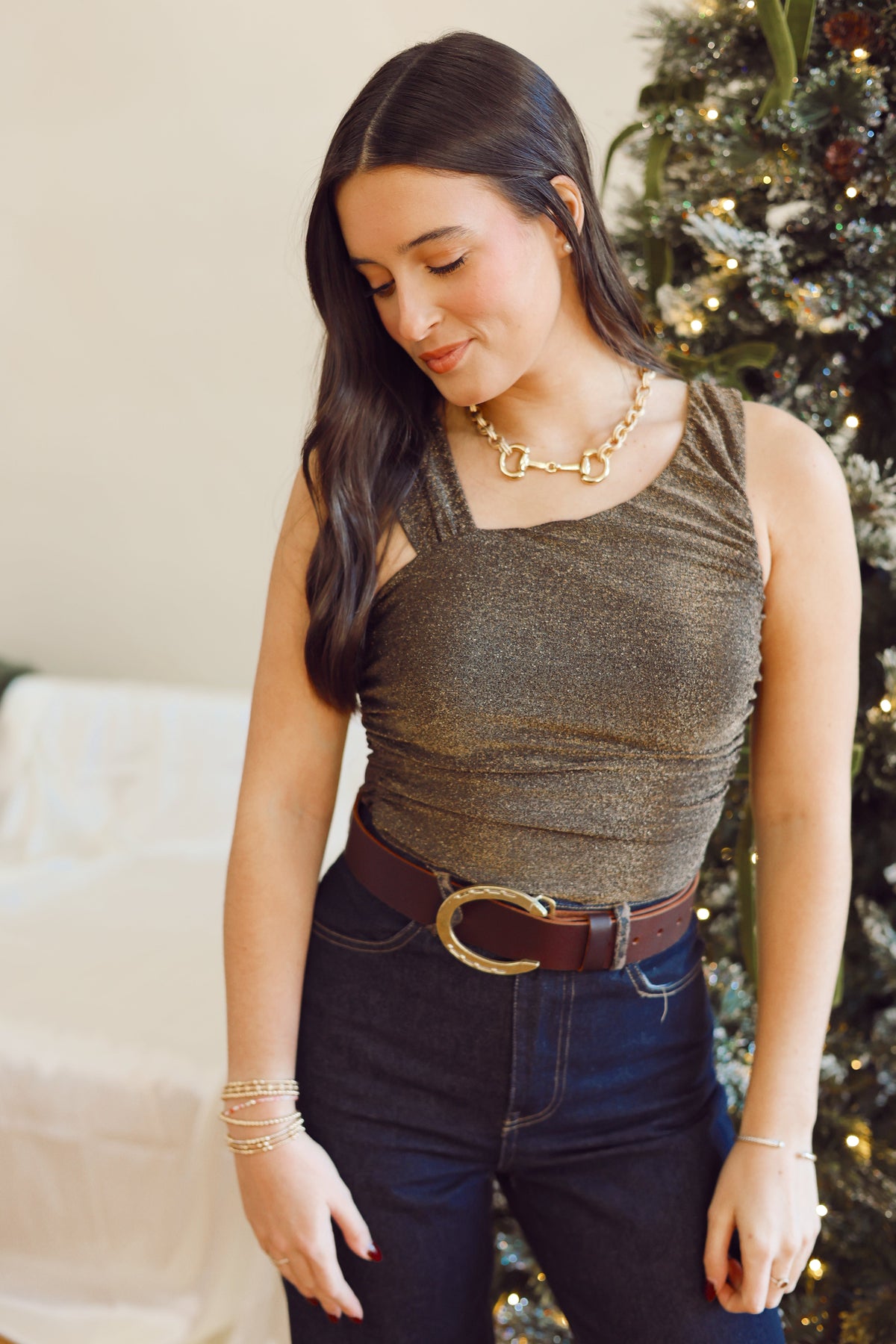 Woman wearing a green top and dark jeans with a Christmas tree in the background