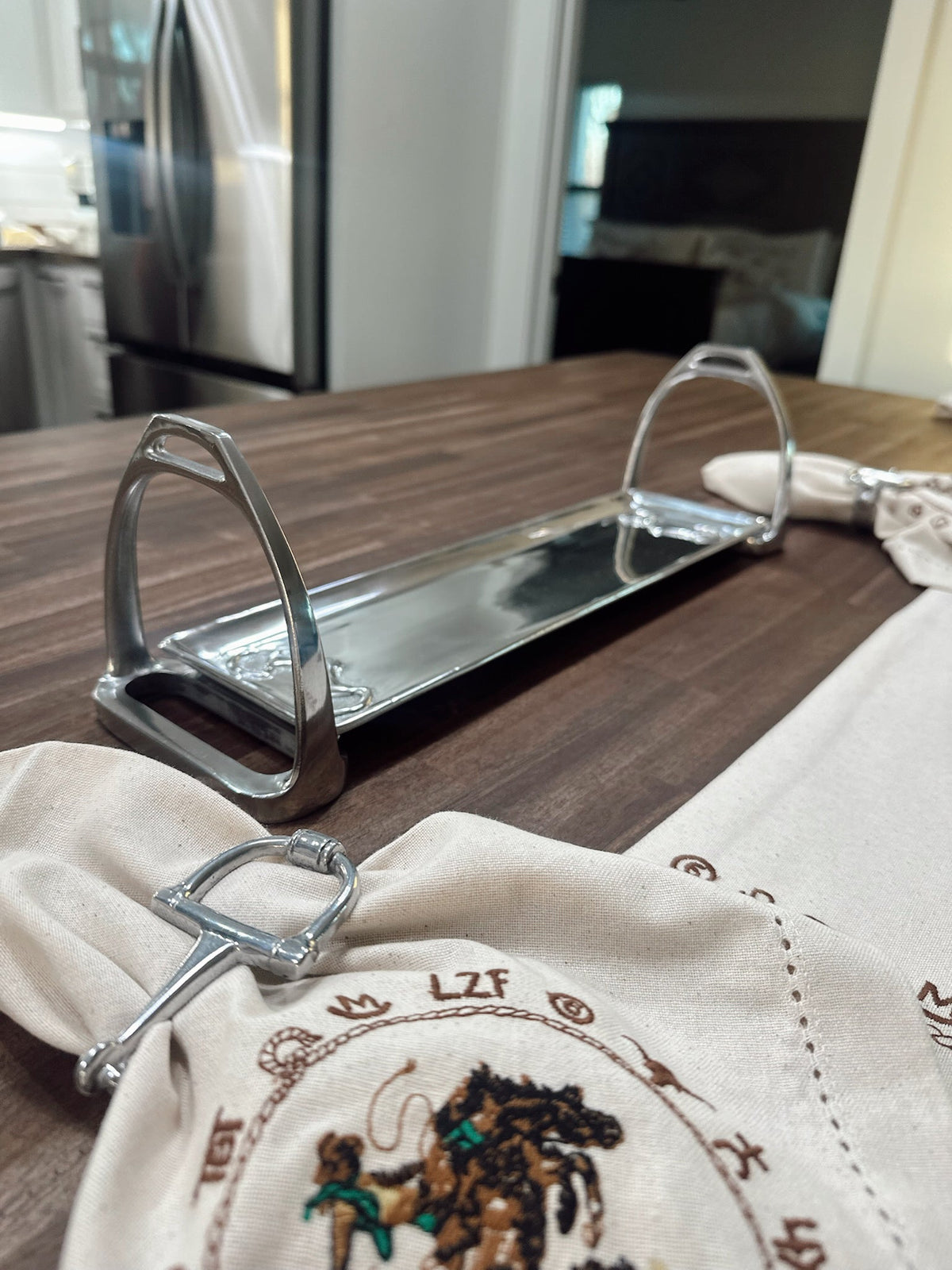 Metal equestrian stirrup napkin holder on a wooden table with embroidered napkins.
