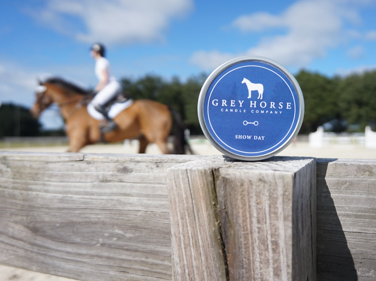 Grey Horse Candle Company container on a wooden post with a horse and rider in the background