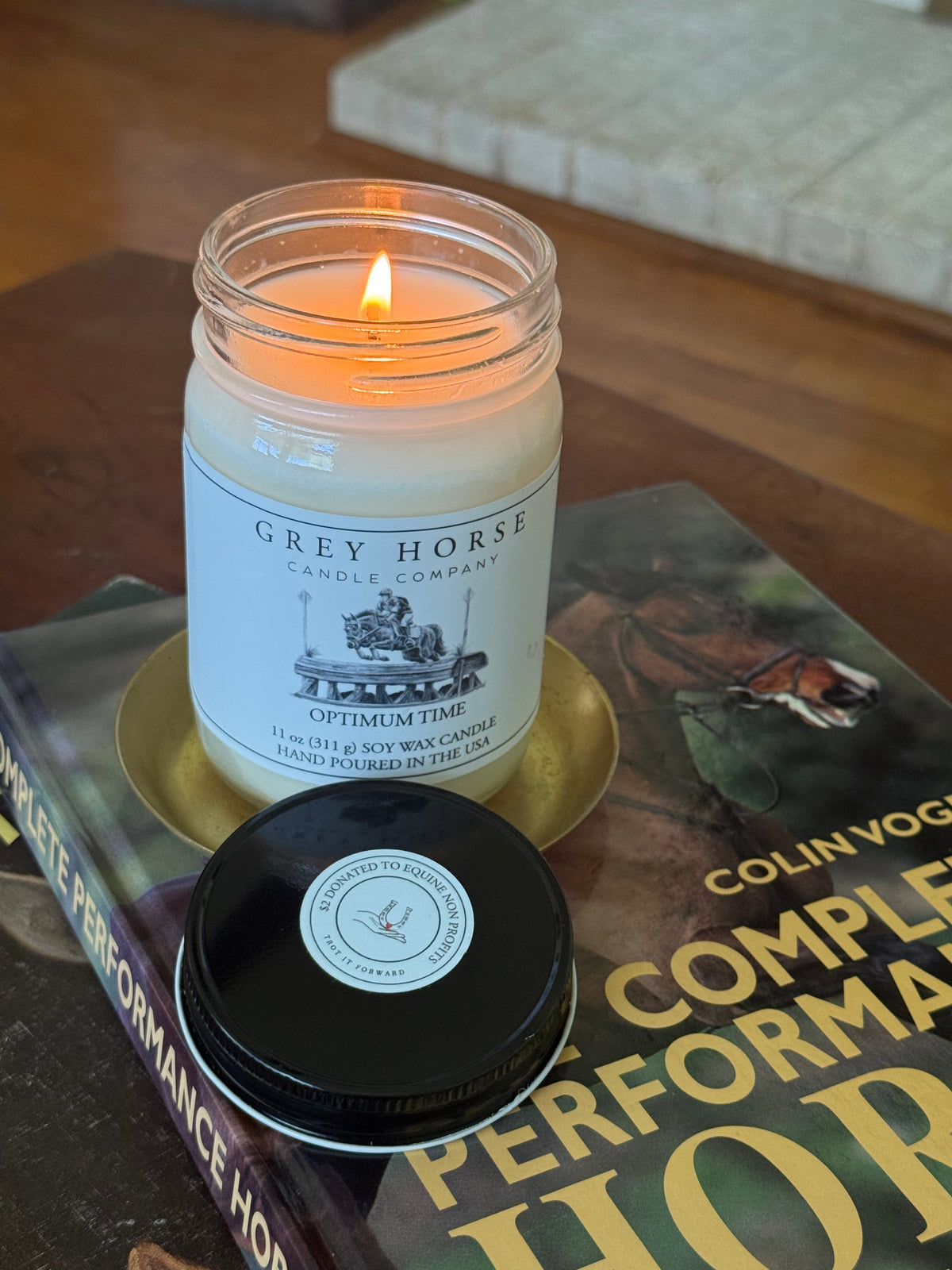 Candle in a jar labeled 'Grey Horse Candle Company' on top of a book