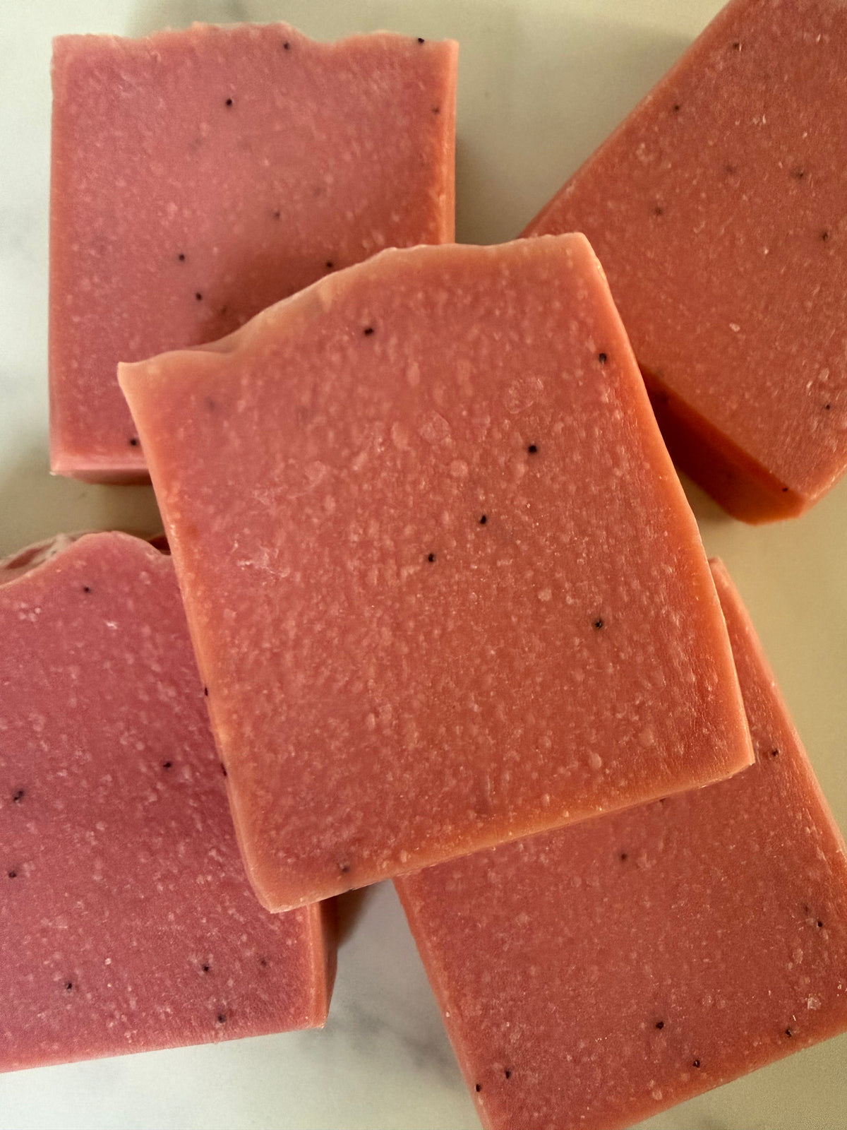 Several rectangular bars of pink soap with small black specks, arranged on a light marble-like surface.