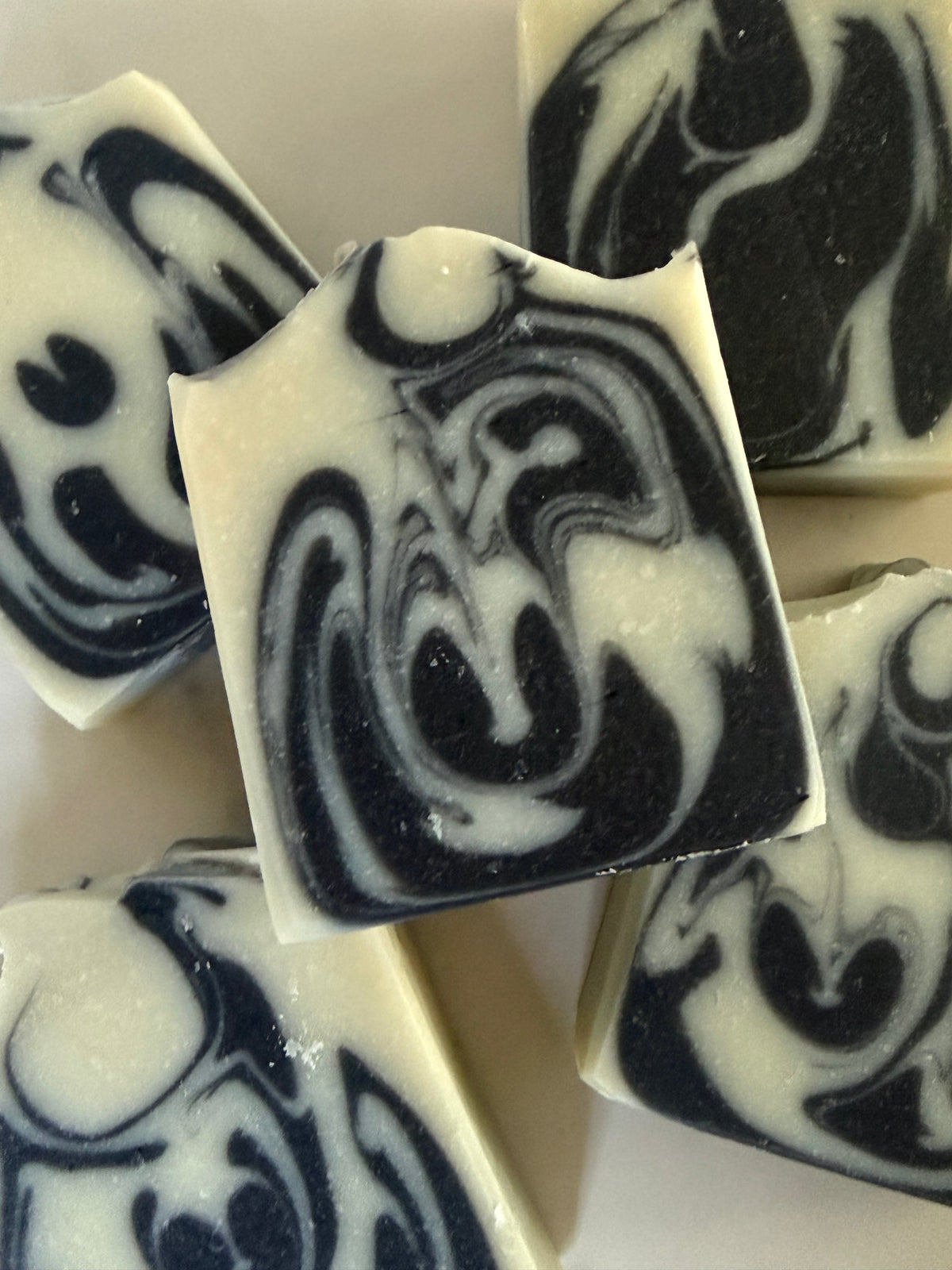 Close-up of several rectangular bars of marbled soap with a black and off-white swirl pattern, arranged on a light neutral background.