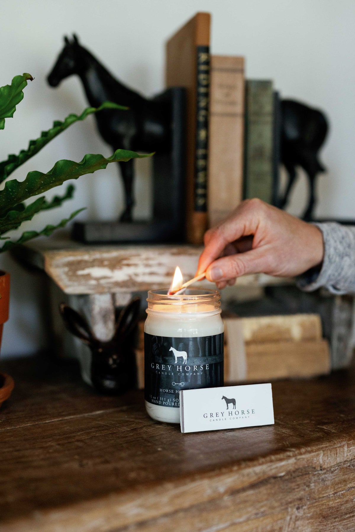 Person lighting a candle with a visible brand label on a wooden surface.