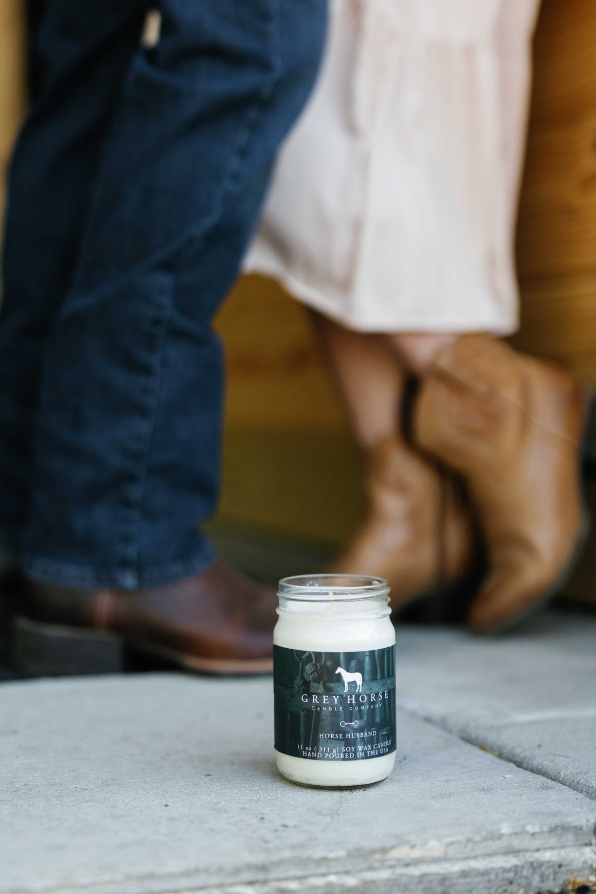 Jar of cream with a label on a concrete surface, with people's legs and feet in the background.