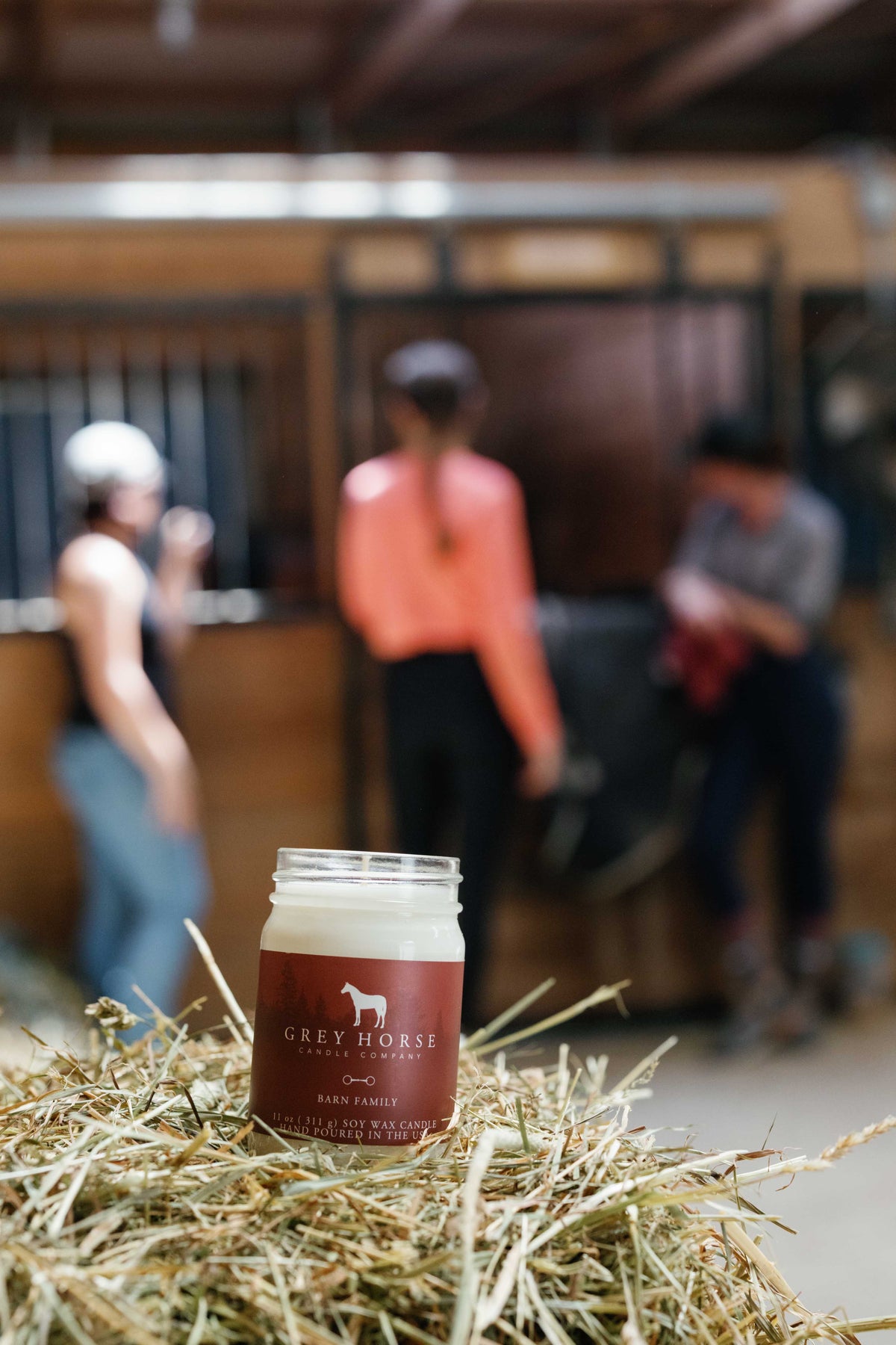 Jar of Grey Horse Creamery product on a bed of hay with people in the background
