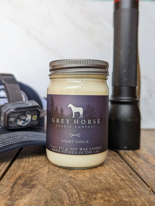 Jar of Grey Horse Candle Company candle on a wooden surface with a flashlight and cap in the background.