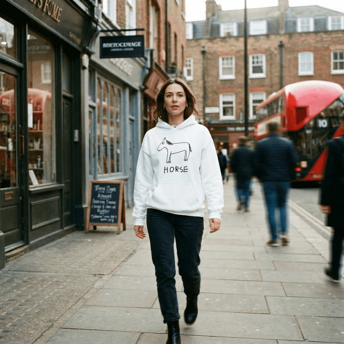 Woman walking on a city street wearing a hoodie with a horse graphic.