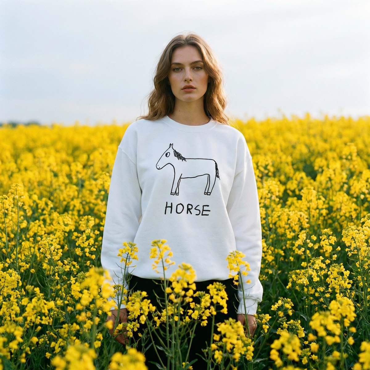 Woman wearing a white sweatshirt with a horse graphic and 'Horse' text in a field of yellow flowers.