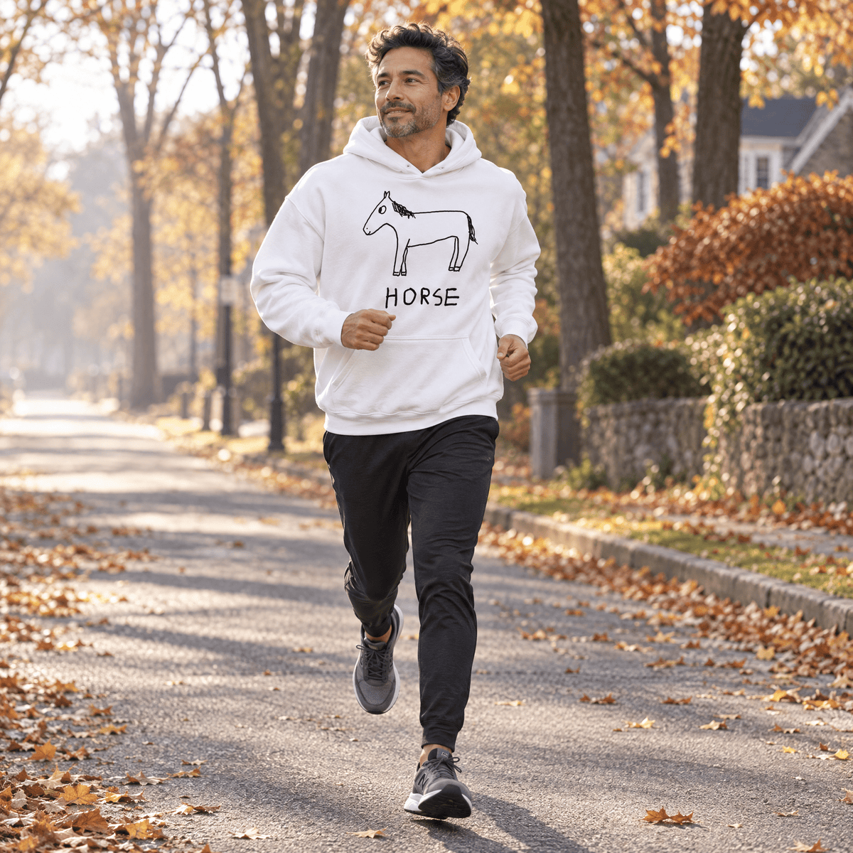 A man jogging on an autumn tree-lined path wearing a white hoodie with a black horse graphic and the word 'HORSE' on the front, paired with black running pants and gray running shoes.