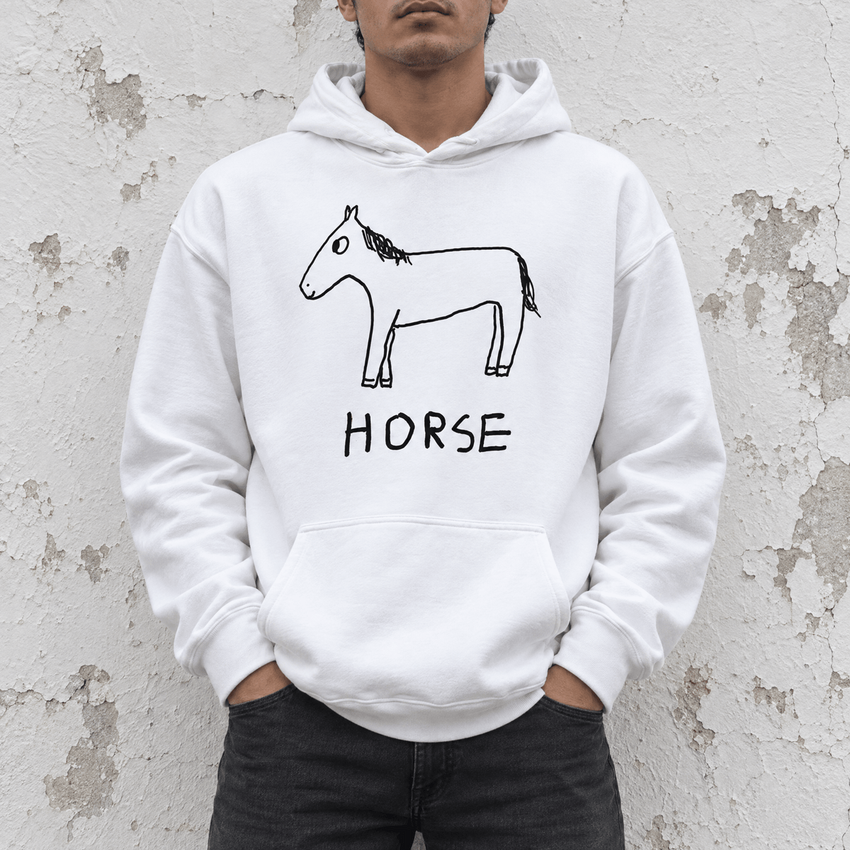 A man wearing a white pullover hoodie with a black line art drawing of a horse and the word 'HORSE' printed on the front, standing against a textured, peeling-stone wall.