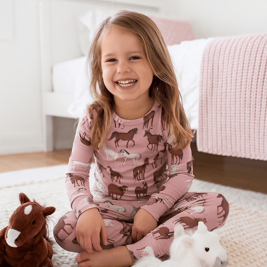 Child wearing pink pajamas with animal patterns, sitting on a bed with stuffed animals.