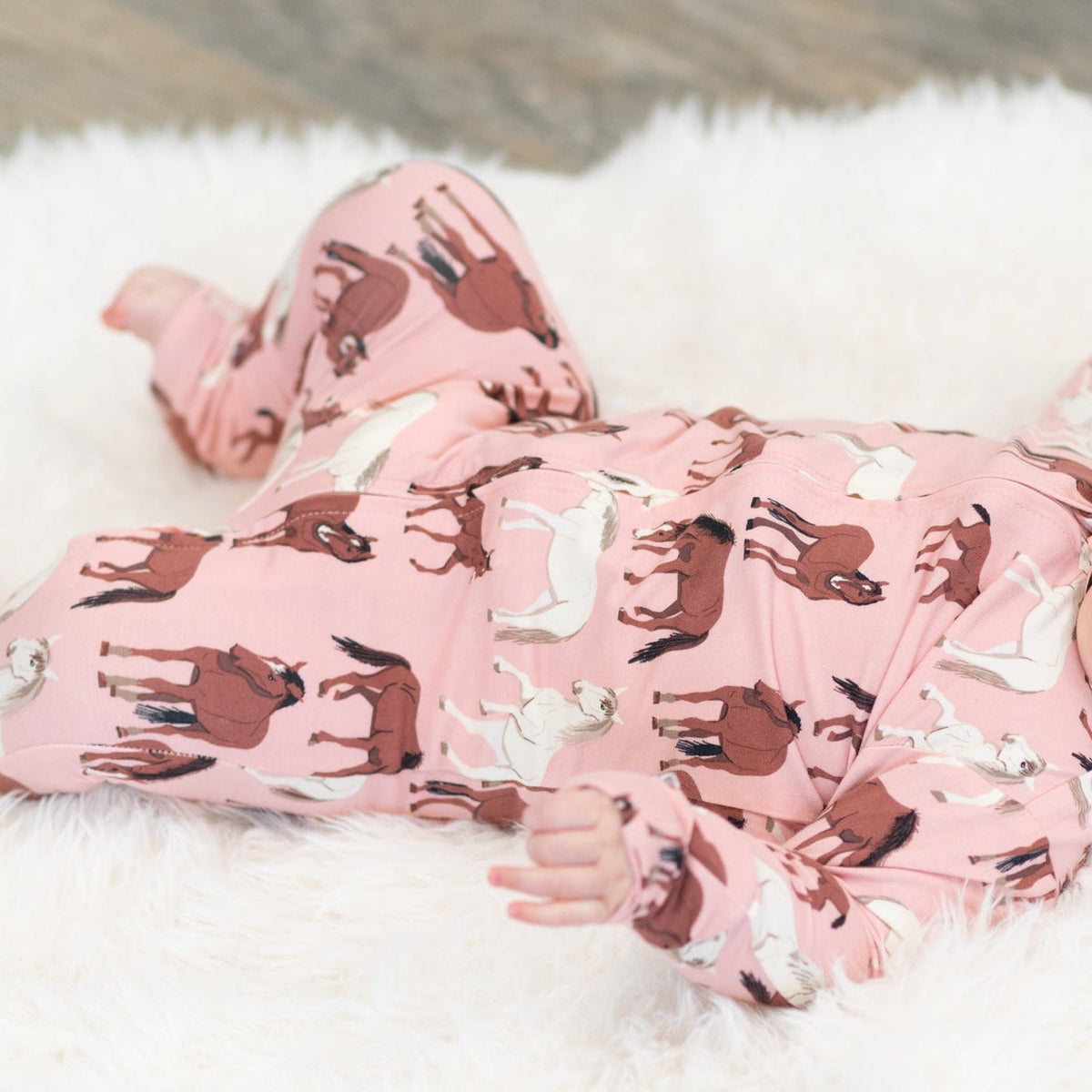 Child wearing pink pajamas with horse patterns on a fluffy white surface